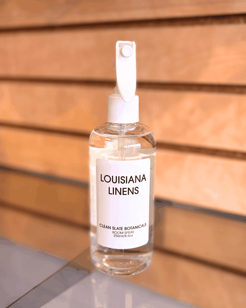 Louisiana Linens clear plastic room spray bottle with white label and white spray nozzle on wooden background