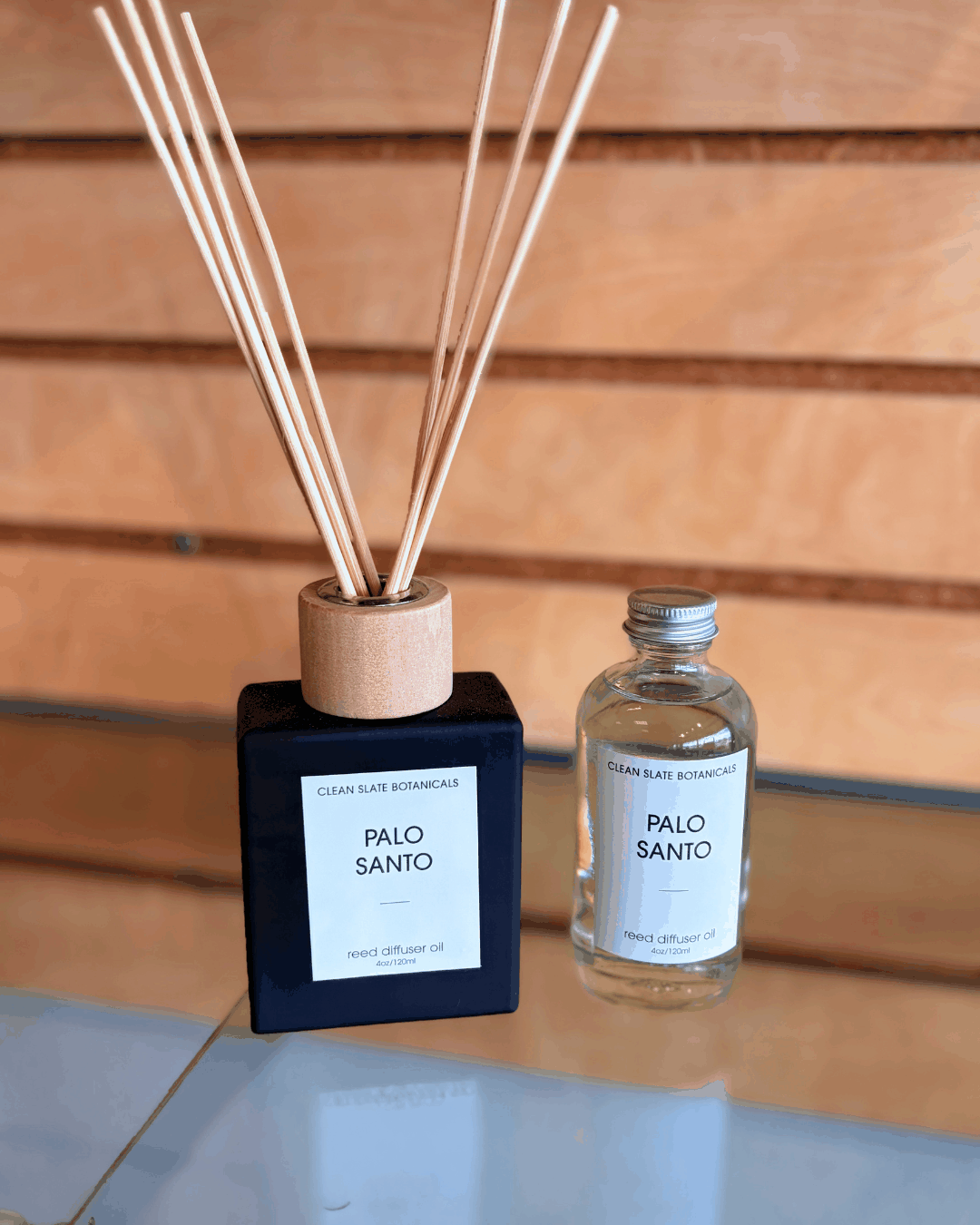 Palo Santo Reed Diffuser set with a matte black square bottle and natural wood cap alongside a clear refill oil bottle, featuring minimalist white labels
