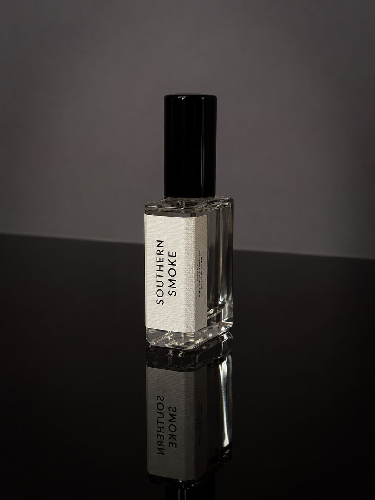 Southern Smoke Wearable Fragrance in a transparent glass bottle with black cap and white label on reflective black surface