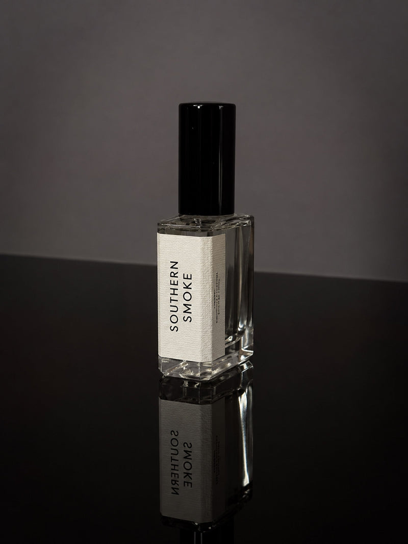 Southern Smoke Wearable Fragrance in a transparent glass bottle with black cap and white label on reflective black surface