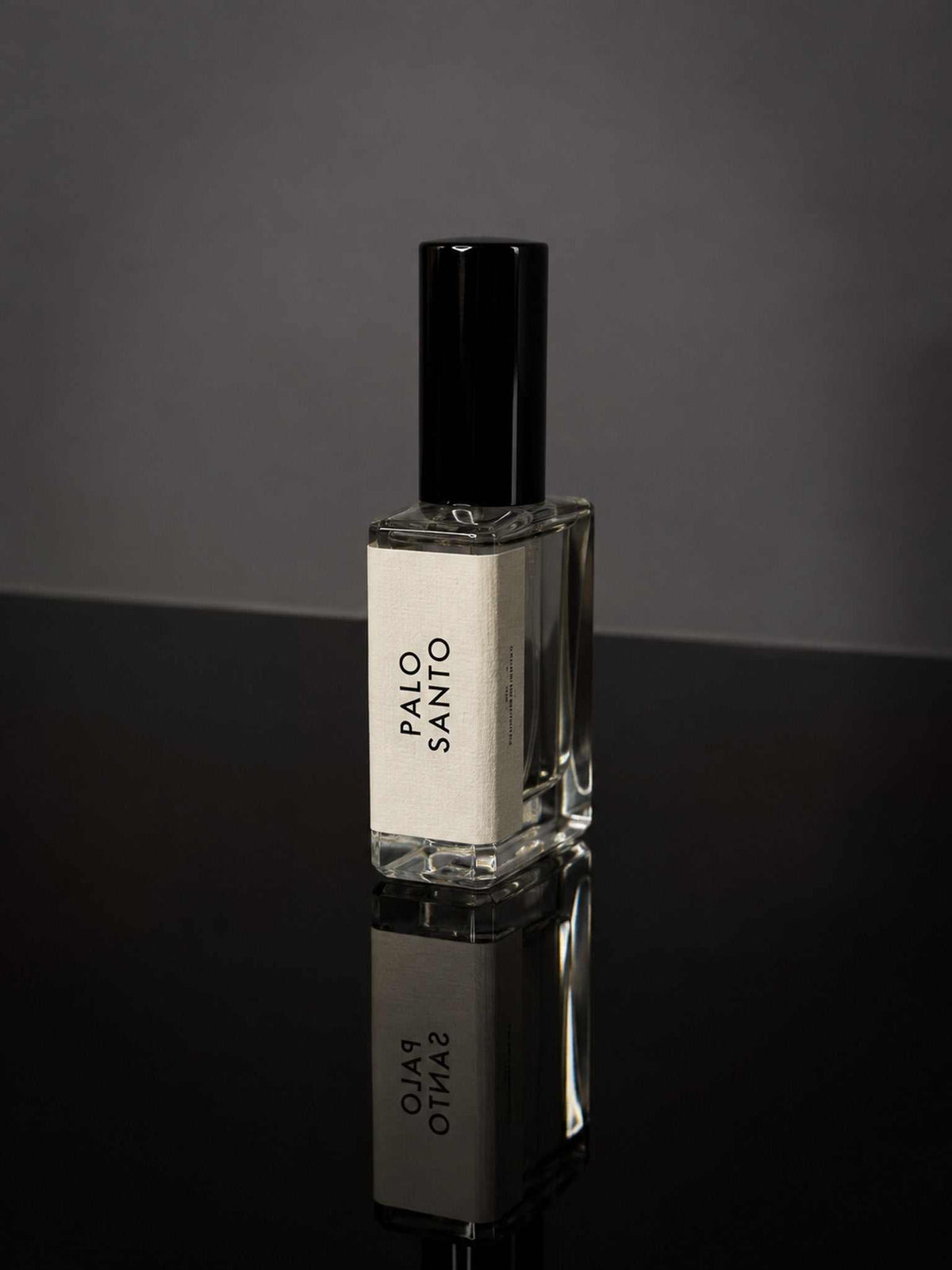 Small clear glass fragrance bottle with black cap and white label reading Palo Santo, presenting woody luxury palo santo scent