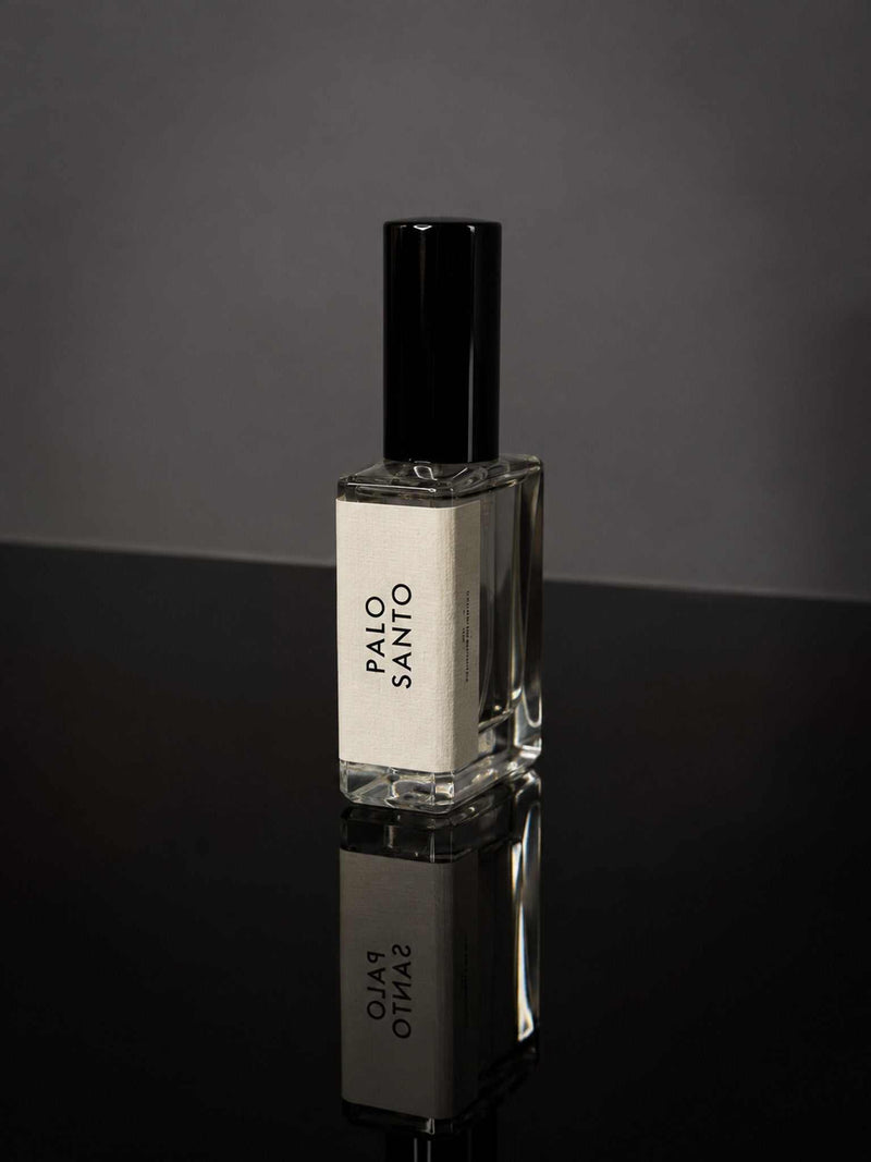 Small clear glass fragrance bottle with black cap and white label reading Palo Santo, presenting woody luxury palo santo scent